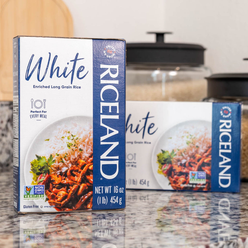 Two boxes of Riceland White Rice on a kitchen counter with jars in the background.