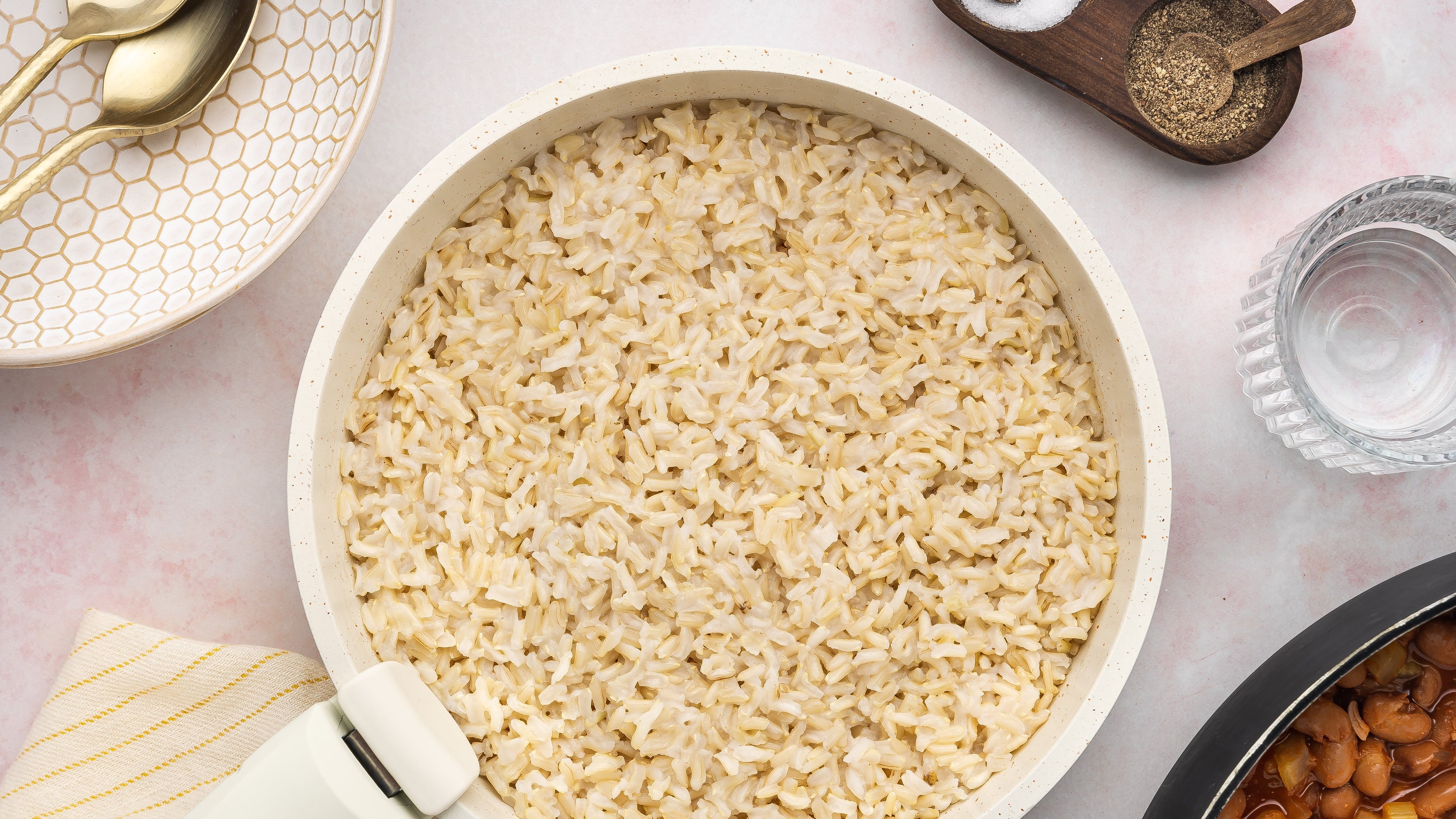 White pan filled with cooked rice on a counter with a pan of rice and a spoon.