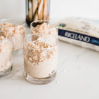 Glass containers with a rice pudding on a kitchen counter with wooden spoons in the background.