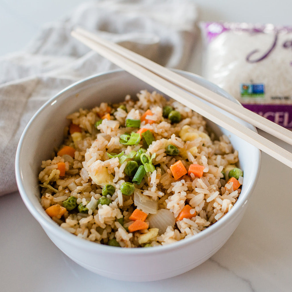 Bowl of fried rice with vegetables and chopsticks, next to a package of Riceland rice on a light background.